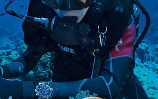 A male scuba diver underwater wearing a diving watch. 
