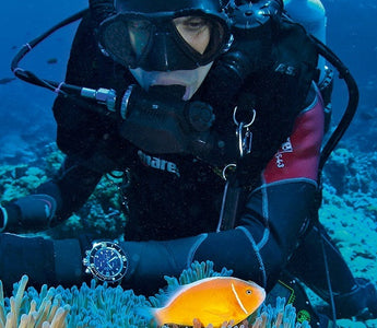 A male scuba diver underwater wearing a diving watch. 