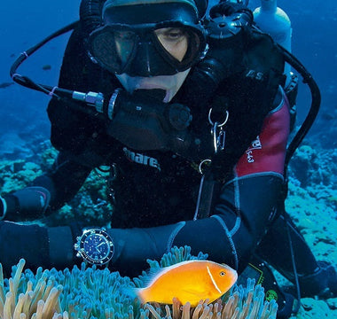 A male scuba diver underwater wearing a diving watch. 