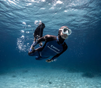A male scuba diver underwater wearing a diving watch. 